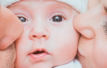 padres primerizos besando a un bebé