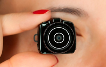 mini cámara de fotos sujeta por una mano con uñas rojas y puesto delante del ojo de una chica como si estuviera espiando