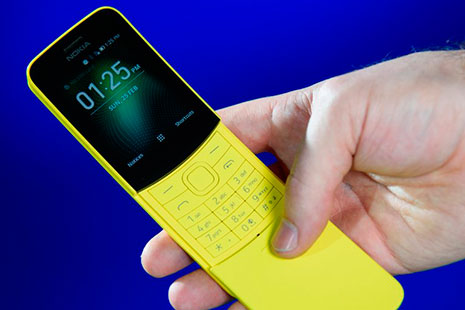 Una mano sostiene el nuevo Nokia 8100 de color amarillo sobre un fondo azul