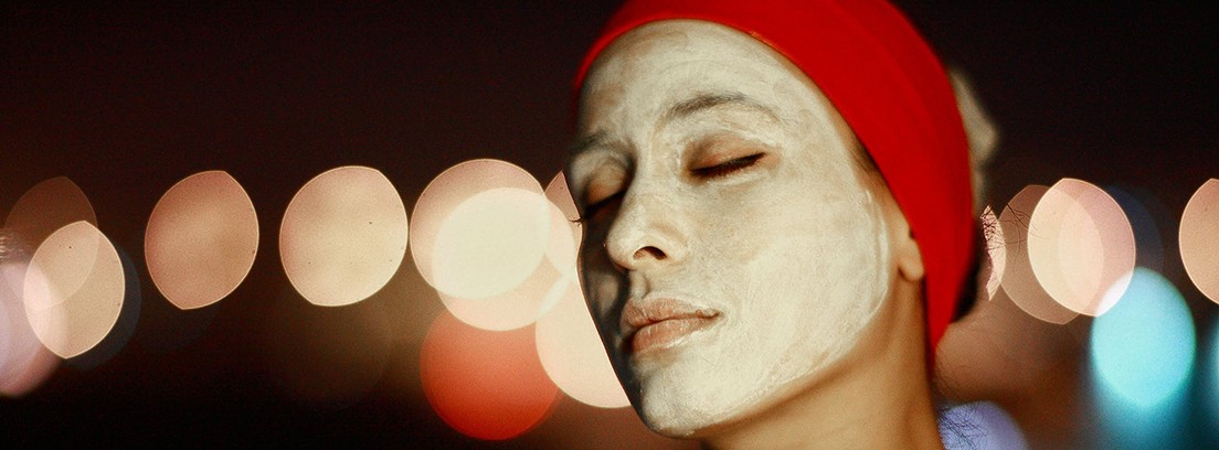 mascarillas faciales caseras efectivas crema facial Mujer con cinta roja sobre el pelo y rostro cubierto de blanco