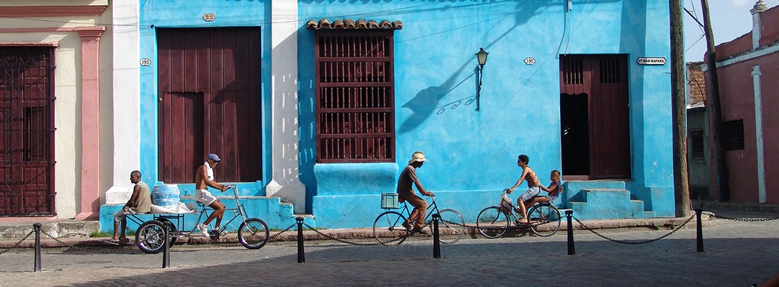 Típica casa cubana con fachada azul y personas montando en bici