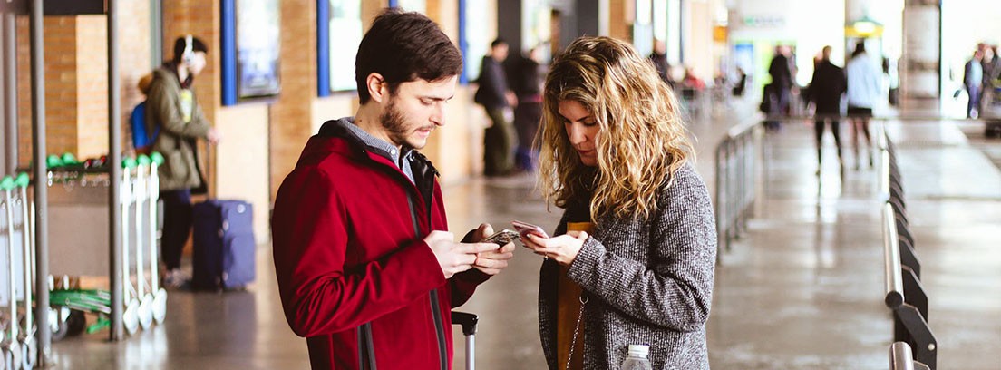mejores apps de turismo para descubrir Hombre y mujer junto a maleta miran las pantallas de sus móviles