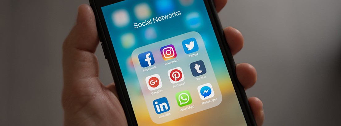 Mano sujeta un móvil con la pantalla encendida y logos de diversas apps sociales