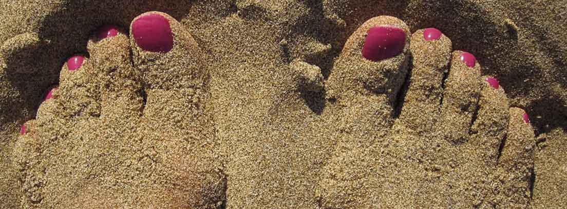 Pies con uñas rosas pintadas y parcialmente cubiertos de arena fina y dorada