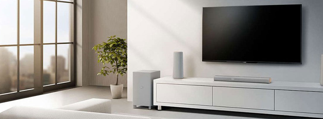 Hombre y mujer sentados frente a un televisor con una barra de sonido sobre mueble blanco