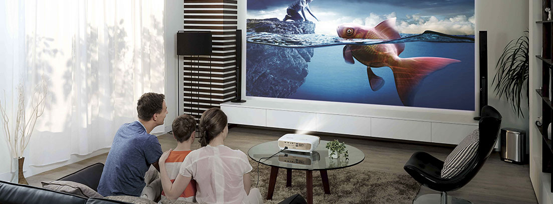 Hombre mujer y niño sentados de espaldas en un sofá frente a un televisor modero con un niño y un pez en la pantalla