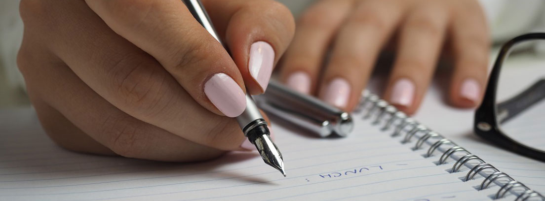 Manos con las uñas rosas y pluma escribiendo sobre un cuaderno