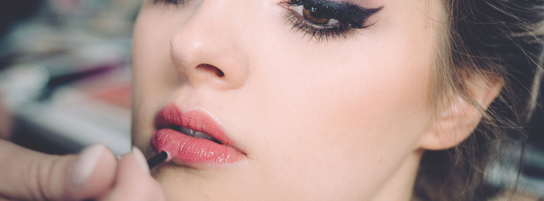 Rostro de mujer con ojos pintados y mano con pincel sobre los labios