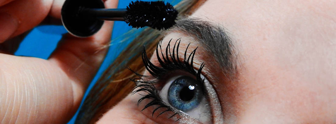 Primer plano de ojo de una mujer aplicando máscara con un cepillo de pestañas