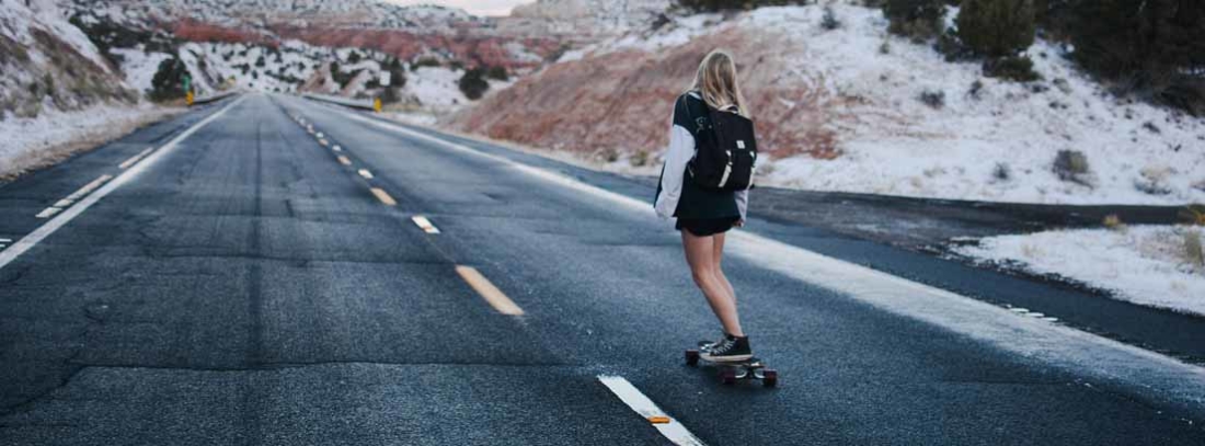 chica con su tabla de skate circulando por una carretera
