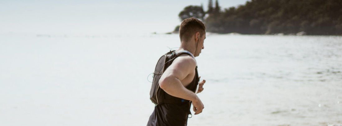 Hombre corriendo por la orilla de la playa con cascos.