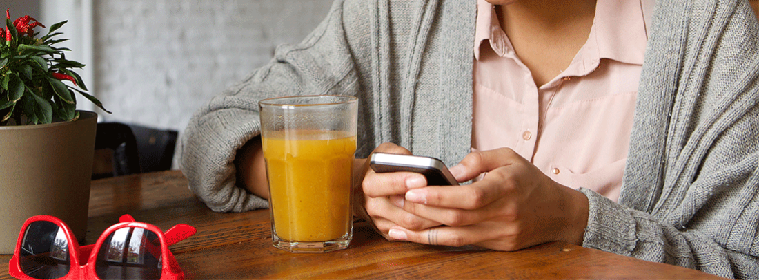 Cómo pasar datos de un móvil a otro - generacionYOUNG mujer tomando un zumo de naranja mientras mira su móvil