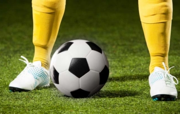 Piernas de futbolista con equipación amarilla y un balón entre los pies