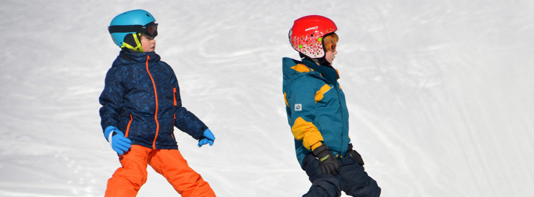 Dos niños sobre la nieve con tablas de esquiar.