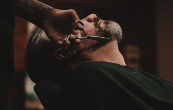 Persona con tijeras sobre la barba de hombre en sillón de barbería